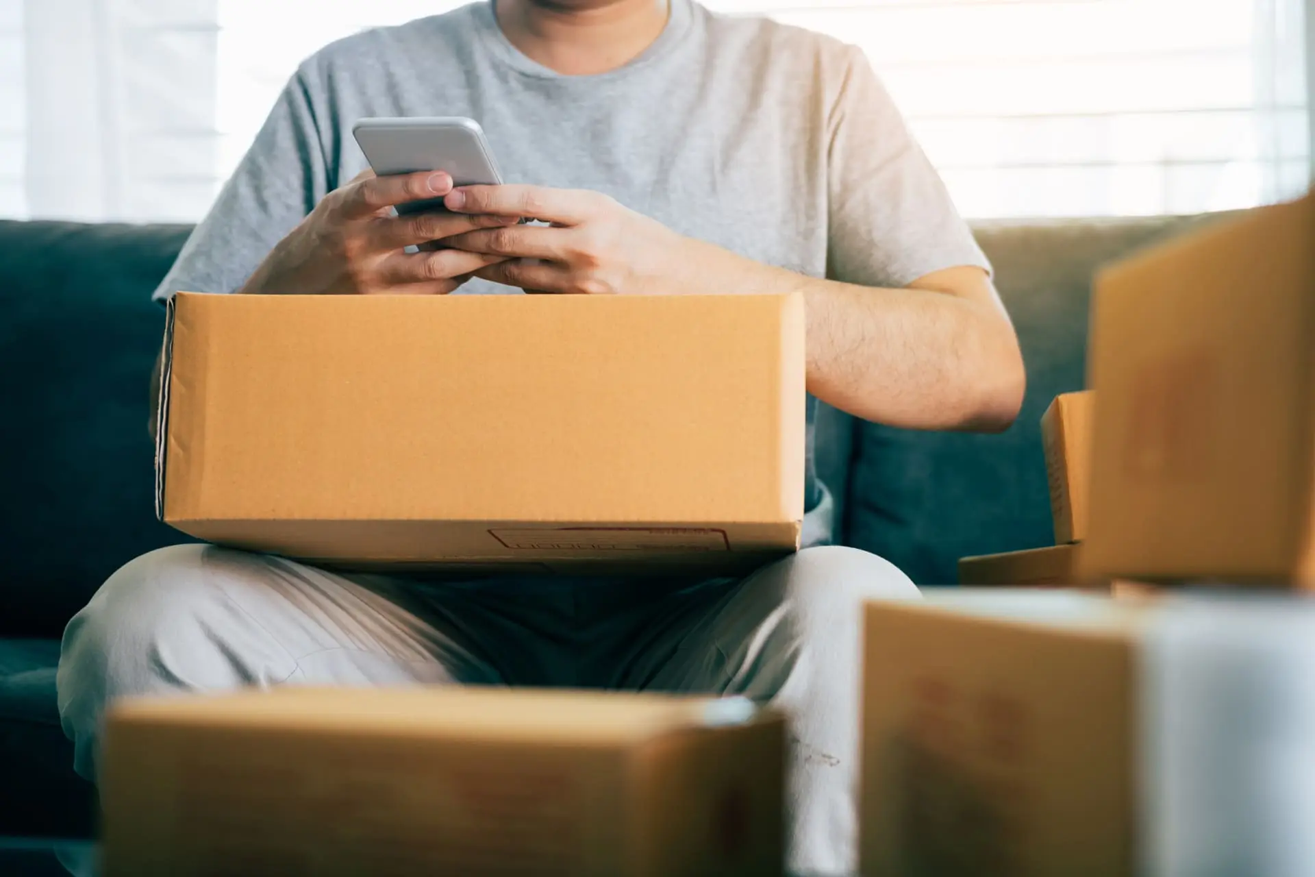 Homme entouré de petits cartons et tenant un téléphone dans les mains